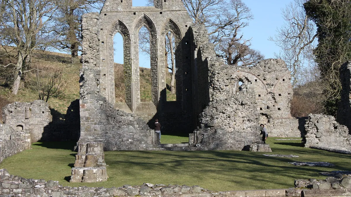 The tall lancet windows of the ruined church at Inch Abbey, with low walls in the grass in front