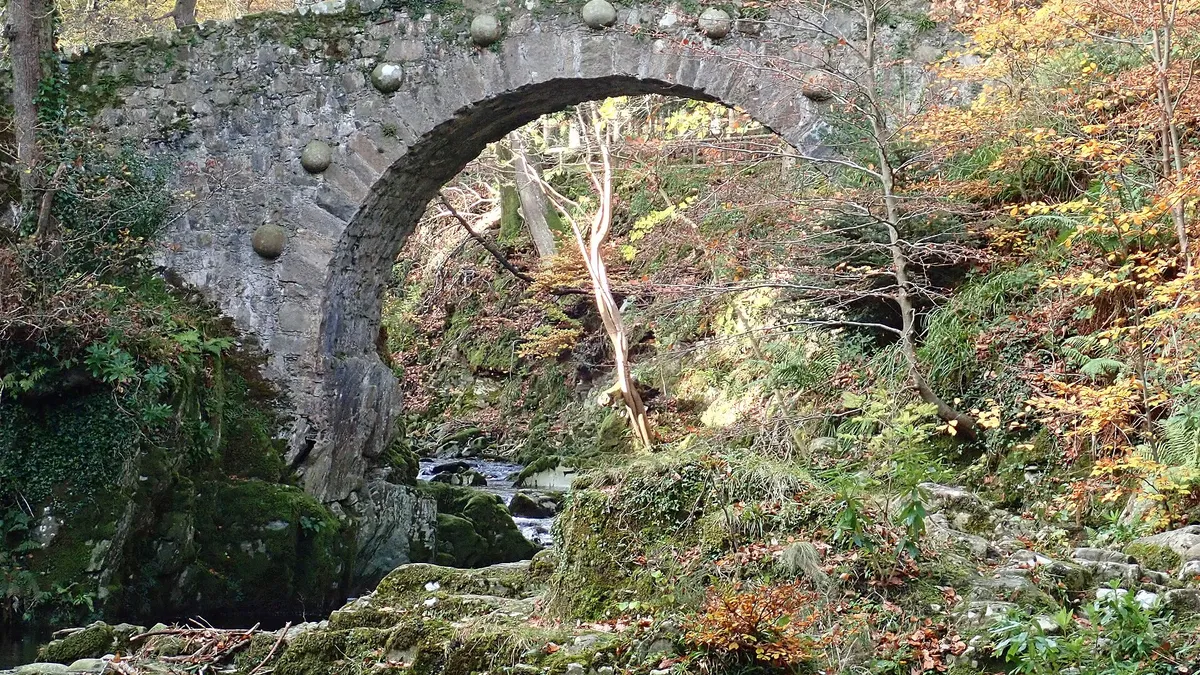 An old stone arch bridge over a river gorge among autumn trees in Tollymore Forest Park