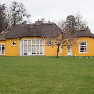Derrymore House, a yellow thatched cottage with wide windows, across a lawn