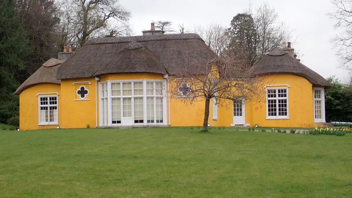 Derrymore House, a yellow thatched cottage with wide windows, across a lawn