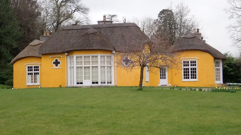 Derrymore House, a yellow thatched cottage with wide windows, across a lawn
