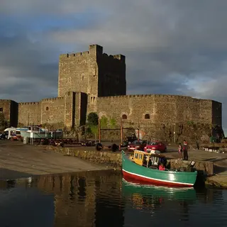 Carrickfergus Castle's keep and curtain wall seen across the harbour, with a fishing boat moored in front