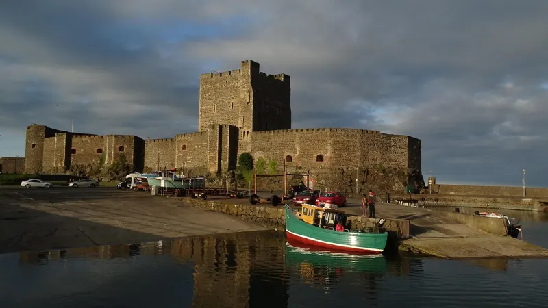 Carrickfergus Castle's keep and curtain wall seen across the harbour, with a fishing boat moored in front