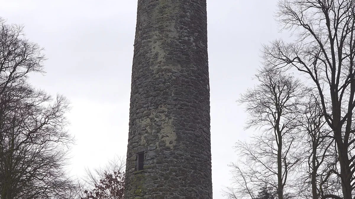 The stone shaft of Antrim Round Tower between bare trees