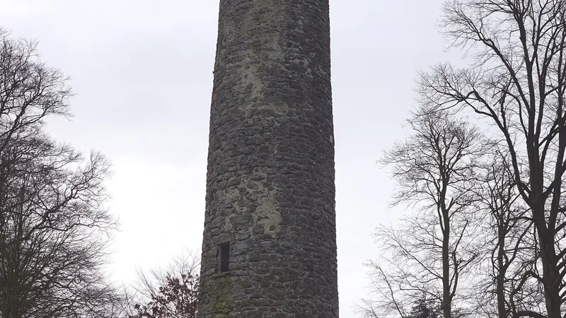 The stone shaft of Antrim Round Tower between bare trees