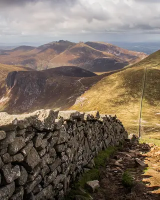 The Mourne Wall running along a grassy ridge, with the peaks of the Mourne Mountains behind it