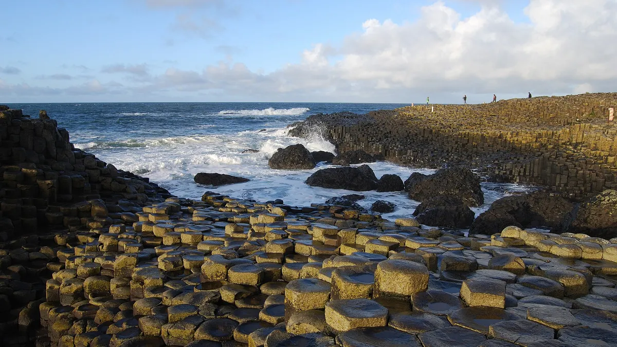 Basalt columns of the Giant's Causeway stepping down into a rough sea under a blue sky