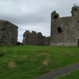 The ruined round keep and curtain wall of Dundrum Castle above a grassy courtyard