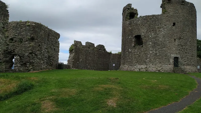 The ruined round keep and curtain wall of Dundrum Castle above a grassy courtyard