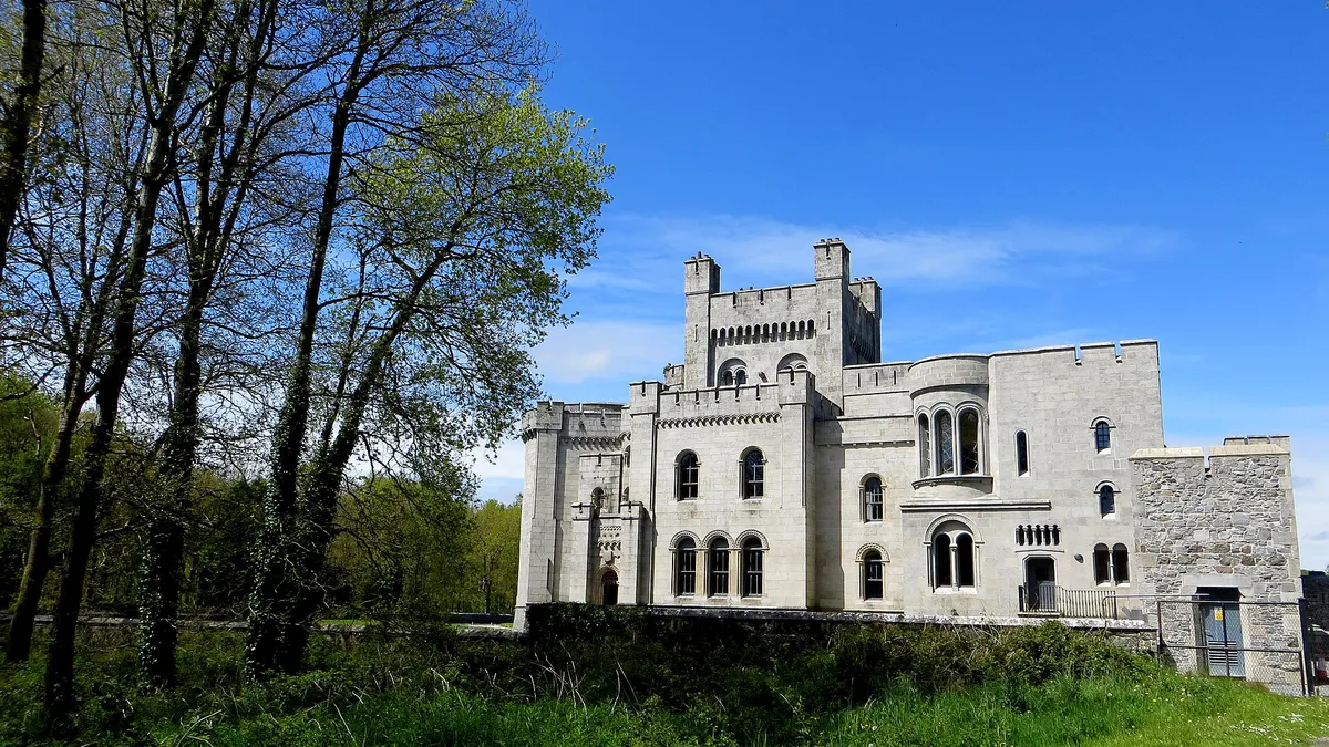 The pale granite towers of Gosford Castle seen through trees under a blue sky