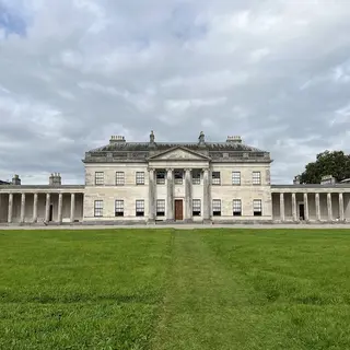The long pale front of Castle Coole with its columned portico and colonnaded wings across a lawn