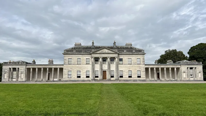 The long pale front of Castle Coole with its columned portico and colonnaded wings across a lawn