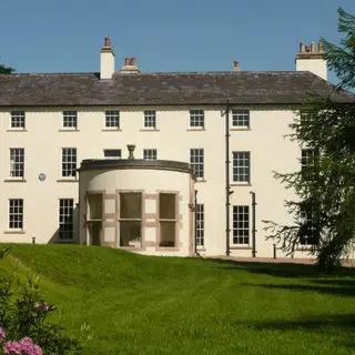 The long cream front of Lissan House with a rounded bay, seen across a lawn with a flowering shrub
