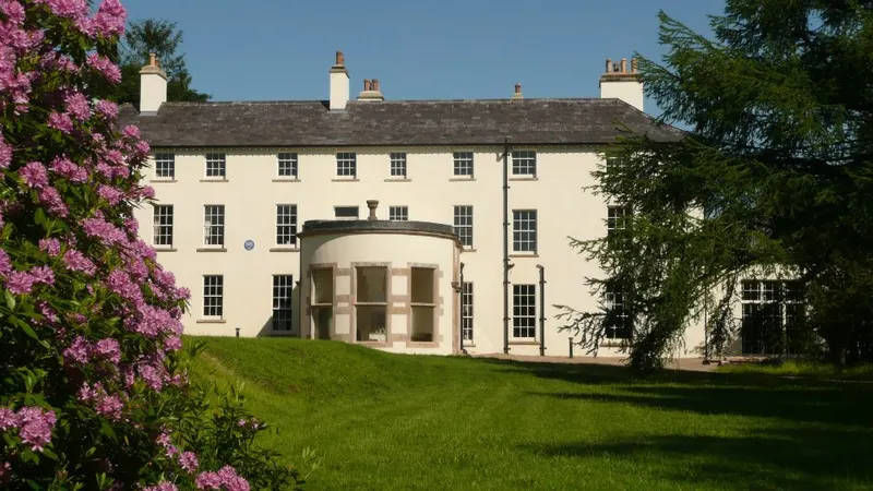 The long cream front of Lissan House with a rounded bay, seen across a lawn with a flowering shrub