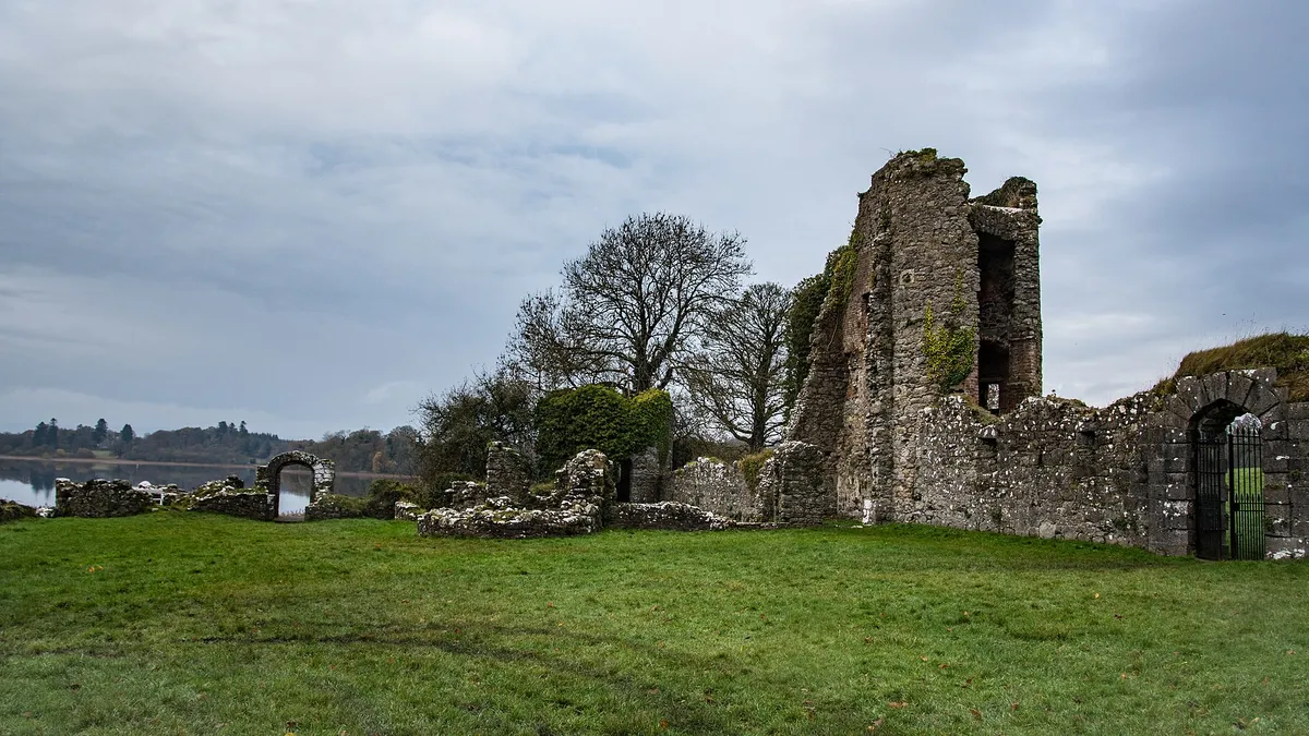 The ruined walls of the old castle at Crom on a lawn with Upper Lough Erne beyond