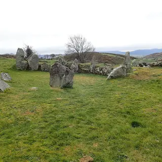 The standing stones of Ballymacdermot court tomb in a grassy field, with low hills behind