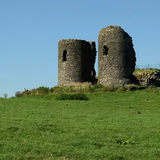 The two ruined round towers of Harry Avery's Castle on a grassy hilltop under a blue sky