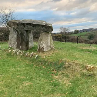 Ballykeel Dolmen, a capstone on three upright stones, at the end of a low cairn in a green field
