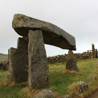 The Legananny Dolmen, a flat capstone raised on three tall stones, beside a stone wall and track