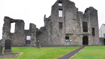The gabled shell of Castle Balfour above a path through the graveyard at Lisnaskea