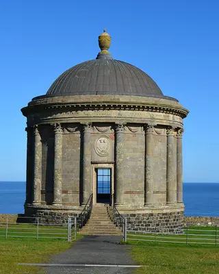 The domed stone Mussenden Temple on its clifftop lawn against a blue sky and sea