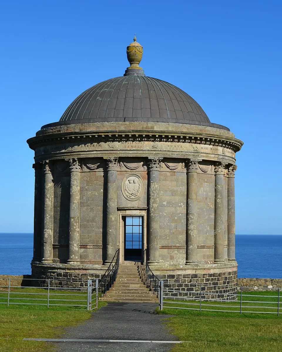 The domed stone Mussenden Temple on its clifftop lawn against a blue sky and sea