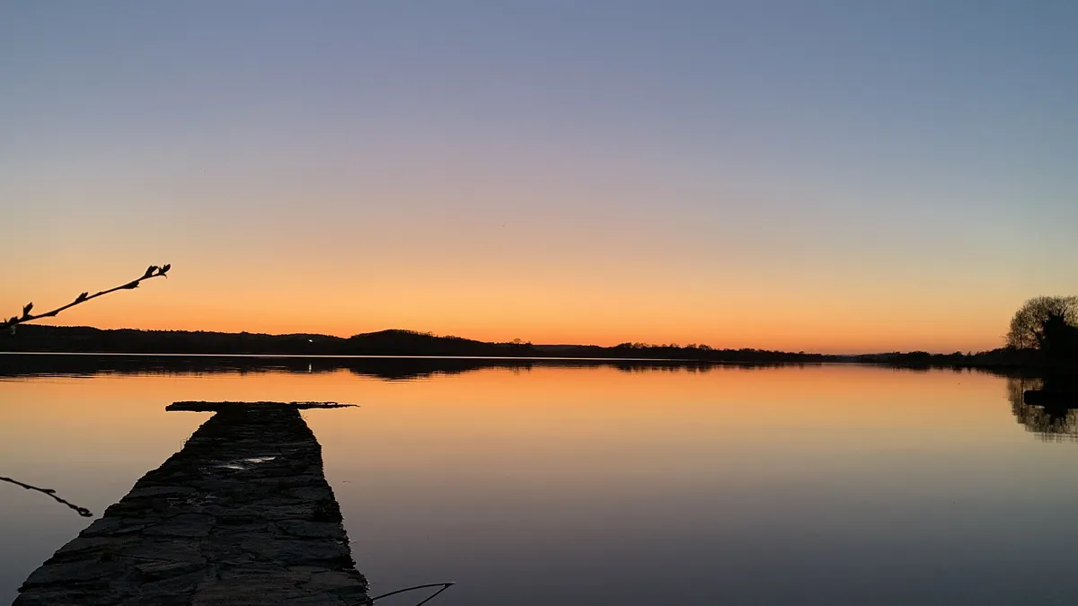 An old stone jetty running out into Lower Lough Erne under an orange evening sky