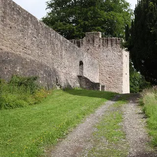 The high stone bawn wall of Benburb Castle and a corner tower beside a grassy track