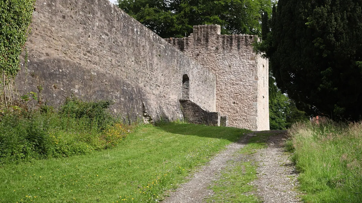 The high stone bawn wall of Benburb Castle and a corner tower beside a grassy track