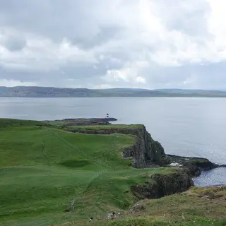 Green clifftops on Rathlin Island running out to a small lighthouse, with the mainland across the water