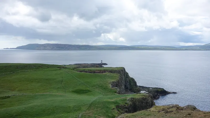 Green clifftops on Rathlin Island running out to a small lighthouse, with the mainland across the water