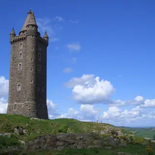 Scrabo Tower, a tall stone tower with a pointed roof, on a green hilltop under a blue sky