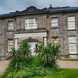 The Argory, a grey stone house with a pillared porch, seen from its gravel drive