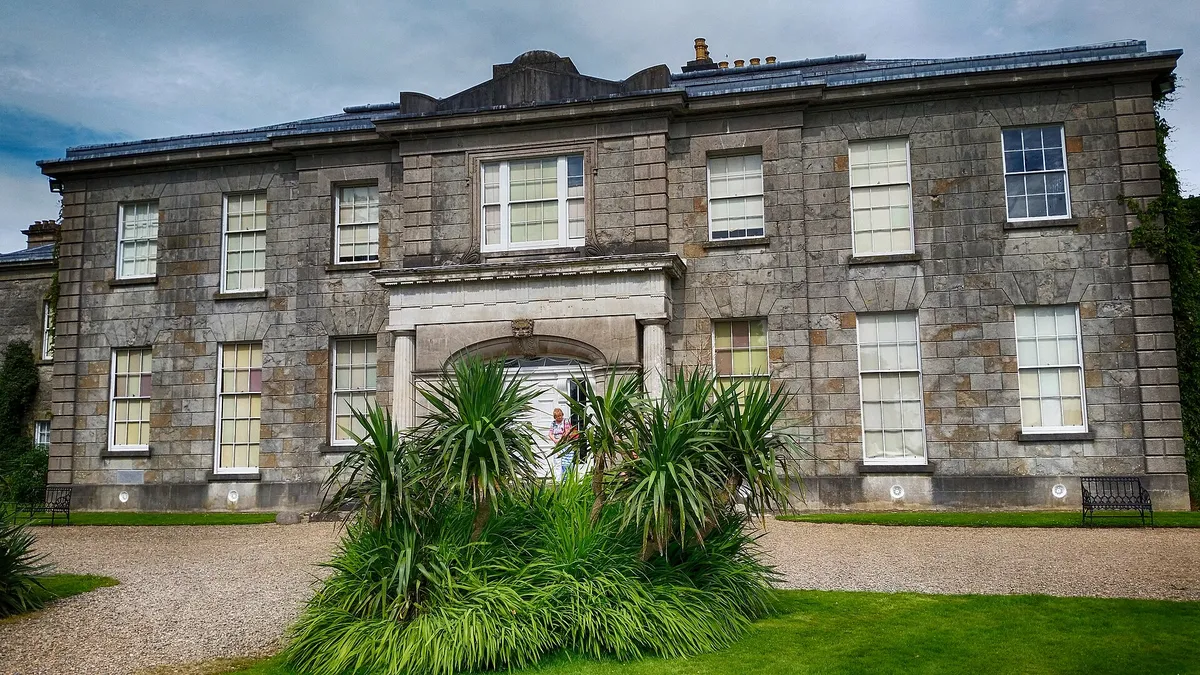 The Argory, a grey stone house with a pillared porch, seen from its gravel drive