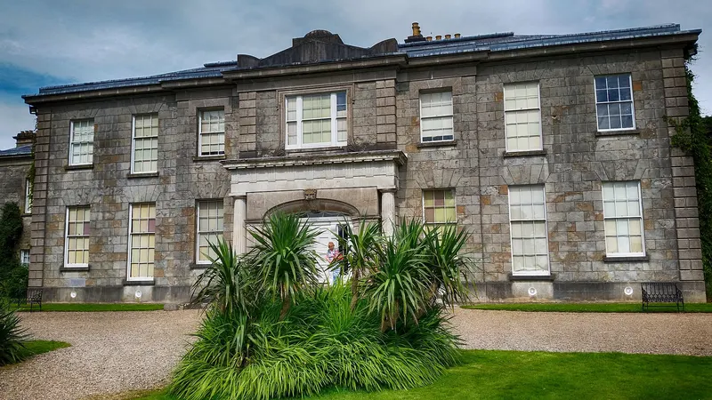 The Argory, a grey stone house with a pillared porch, seen from its gravel drive
