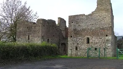 The ruined stone and brick walls of Mountjoy Castle behind a hedge and a green gate