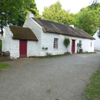 The whitewashed thatched Mellon homestead at the Ulster American Folk Park, with trees around it