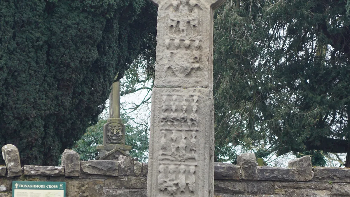 The carved sandstone high cross at Donaghmore on its stepped base in front of a stone wall