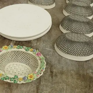 Unfinished woven china bowls and a painted basket with flowers on a workbench at Belleek Pottery