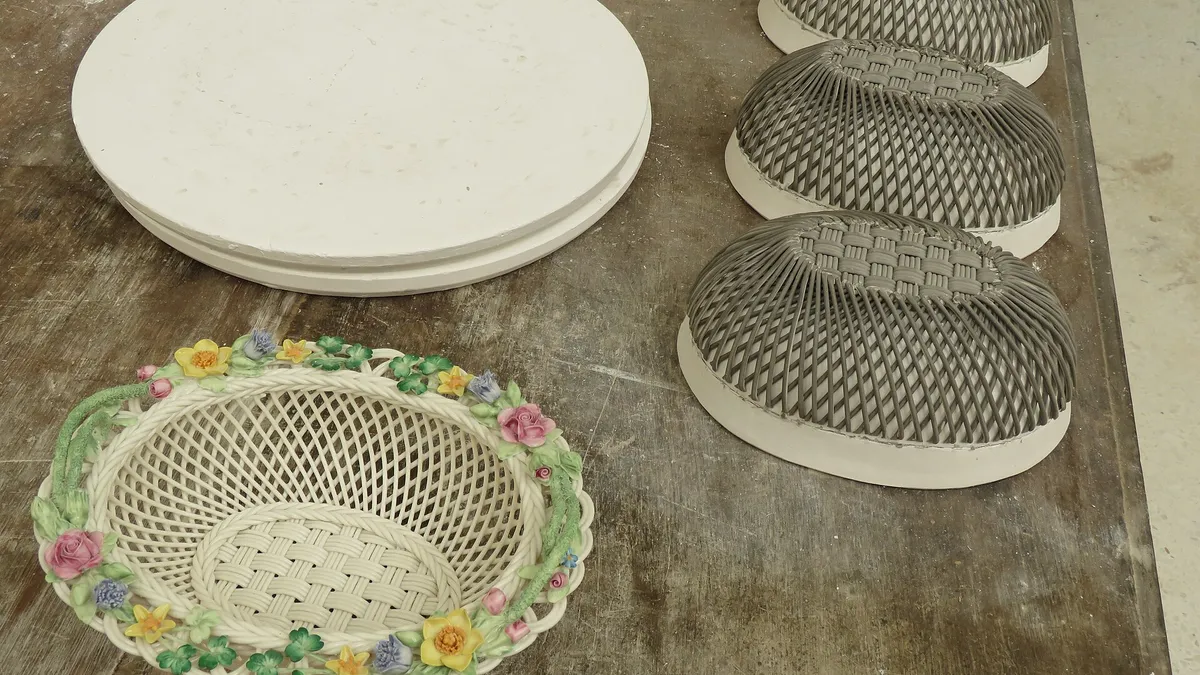Unfinished woven china bowls and a painted basket with flowers on a workbench at Belleek Pottery