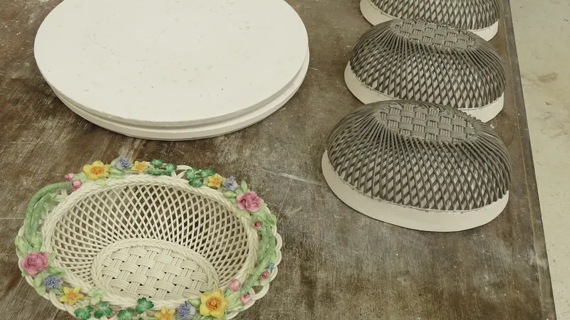 Unfinished woven china bowls and a painted basket with flowers on a workbench at Belleek Pottery