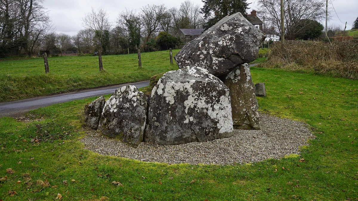 The sloping capstone of Tirnony Dolmen resting on its upright stones beside a country road