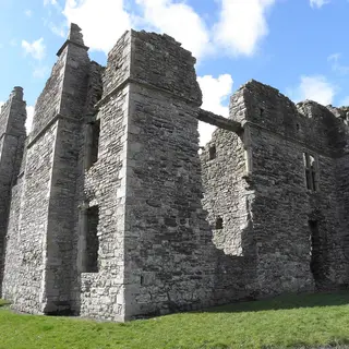 The tall roofless stone walls and chimney stacks of Castle Caulfield above a lawn