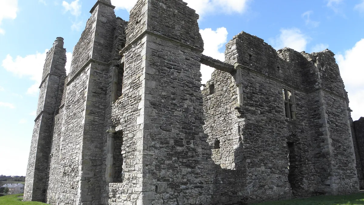 The tall roofless stone walls and chimney stacks of Castle Caulfield above a lawn