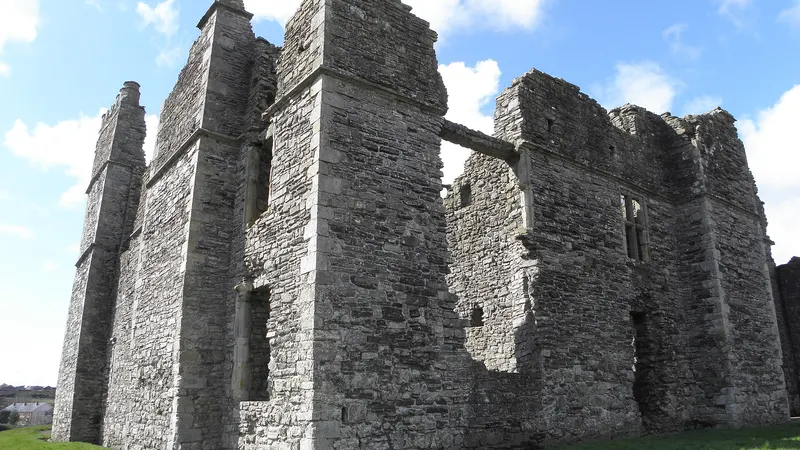 The tall roofless stone walls and chimney stacks of Castle Caulfield above a lawn