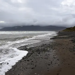 Waves breaking on the dark sand at Murlough, with the Mourne Mountains under cloud across the bay