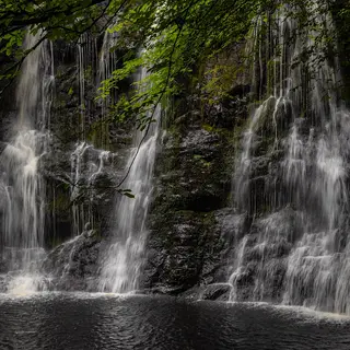 Water falling in several strands over a dark rock ledge into a pool in Glenariff Forest Park