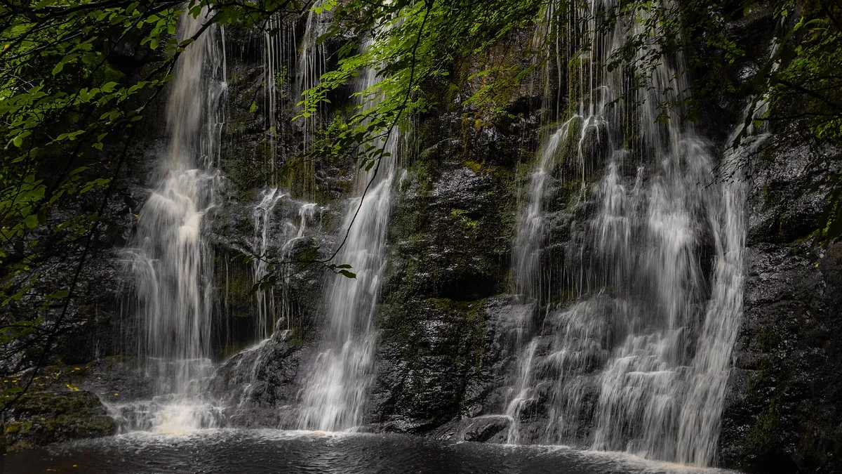 Water falling in several strands over a dark rock ledge into a pool in Glenariff Forest Park