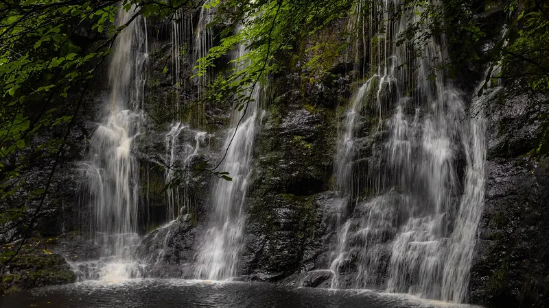Water falling in several strands over a dark rock ledge into a pool in Glenariff Forest Park