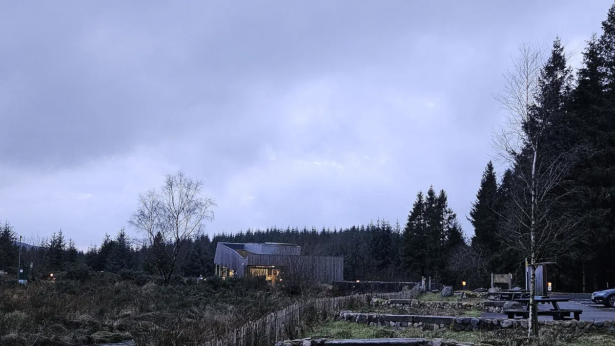 The OM observatory building at dusk in Davagh Forest, with a fenced path and conifers around it